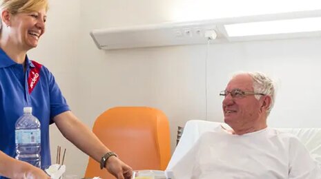 Nurse smiling while caring for an elderly patient resting in a hospital bed.