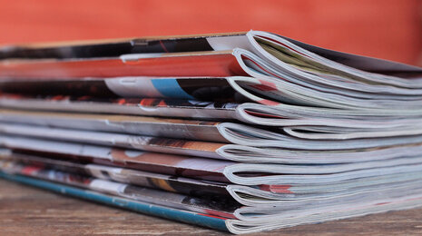 Stack of folded magazines on a wooden surface, symbolizing print media and reading materials