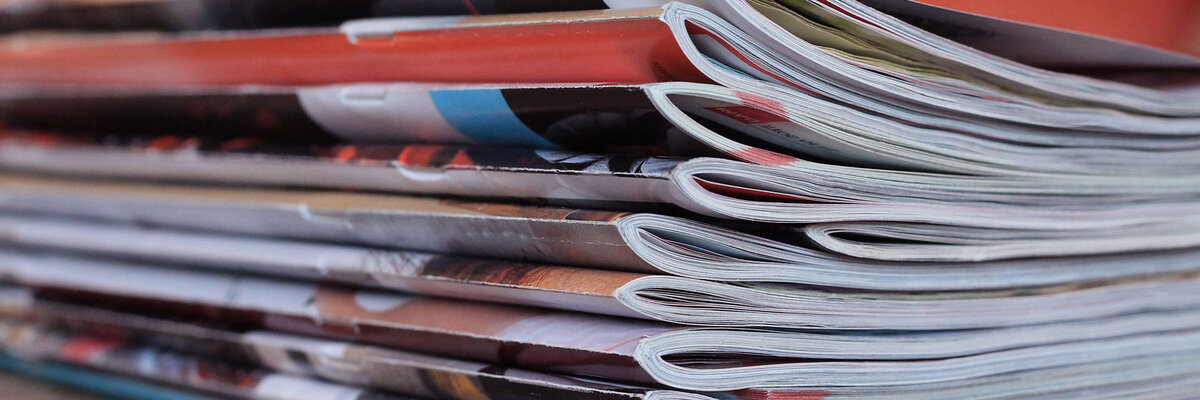 Stack of folded magazines on a wooden surface, symbolizing print media and reading materials