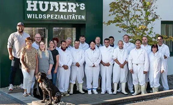 Employees of Huber in white workwear standing together outside a company building.