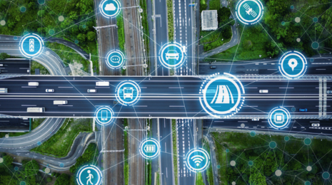 Aerial view of a highway intersection with connected vehicle and smart mobility icons illustrating IoT-based intelligent transportation and digital traffic management.