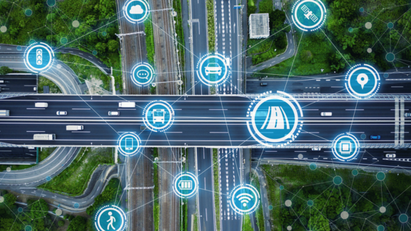 Aerial view of a highway intersection with connected vehicle and smart mobility icons illustrating IoT-based intelligent transportation and digital traffic management.