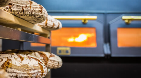 Freshly baked rustic bread loaves cooling on racks in front of a bakery oven.