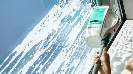 Person cleaning a window using a handheld window-cleaning device from Leifheit.