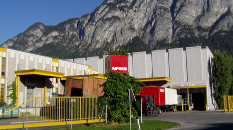 MPREIS logistics and warehouse facility with delivery trucks, set against a mountainous backdrop.