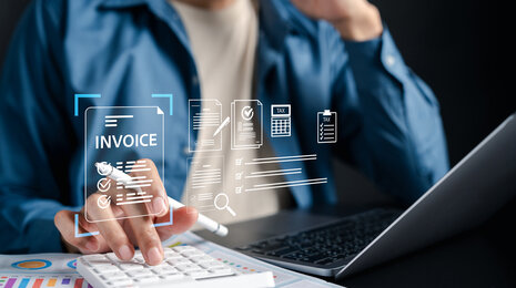 © iStockphoto/champpixs Mitarbeiter nutzt Laptop und Taschenrechner mit digitalen Symbolen für eInvoicing, automatisierte Rechnungsverarbeitung und Steuerdokumente.