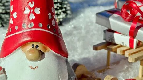 Christmas elf with a red hat holding a gift, sitting by a sled with presents in a snowy landscape