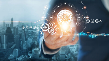 Hand, die eine leuchtende Gl&uuml;hbirne mit digitalen Symbolen h&auml;lt