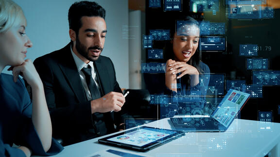 Team of business professionals reviewing data on a laptop and tablet with digital analytics overlays.