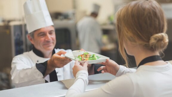 Chef handing a prepared dish to a server in a professional kitchen
