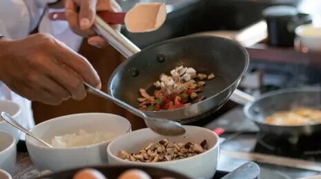 Chef cooking and plating ingredients in a professional kitchen using a frying pan.