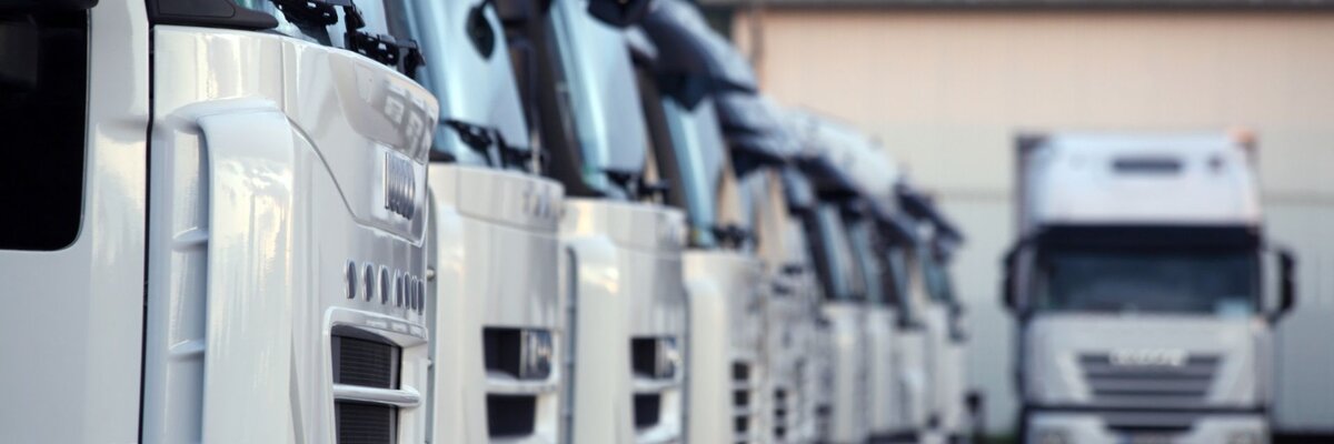 Close-up of a row of white trucks parked in a logistics yard, with one truck in focus in the background, emphasizing fleet management and transportation