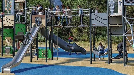 Children playing on a modern playground with slides, climbing frames, and swings.