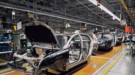 Automotive assembly line with partially assembled car bodies moving along a production conveyor inside a modern factory.