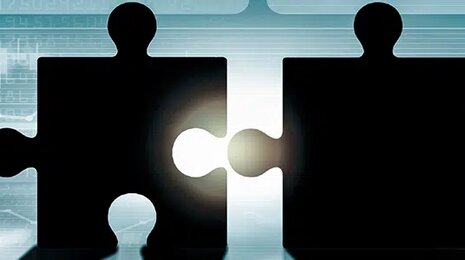 Two businesspeople pushing puzzle pieces together, symbolizing collaboration with digital graphs