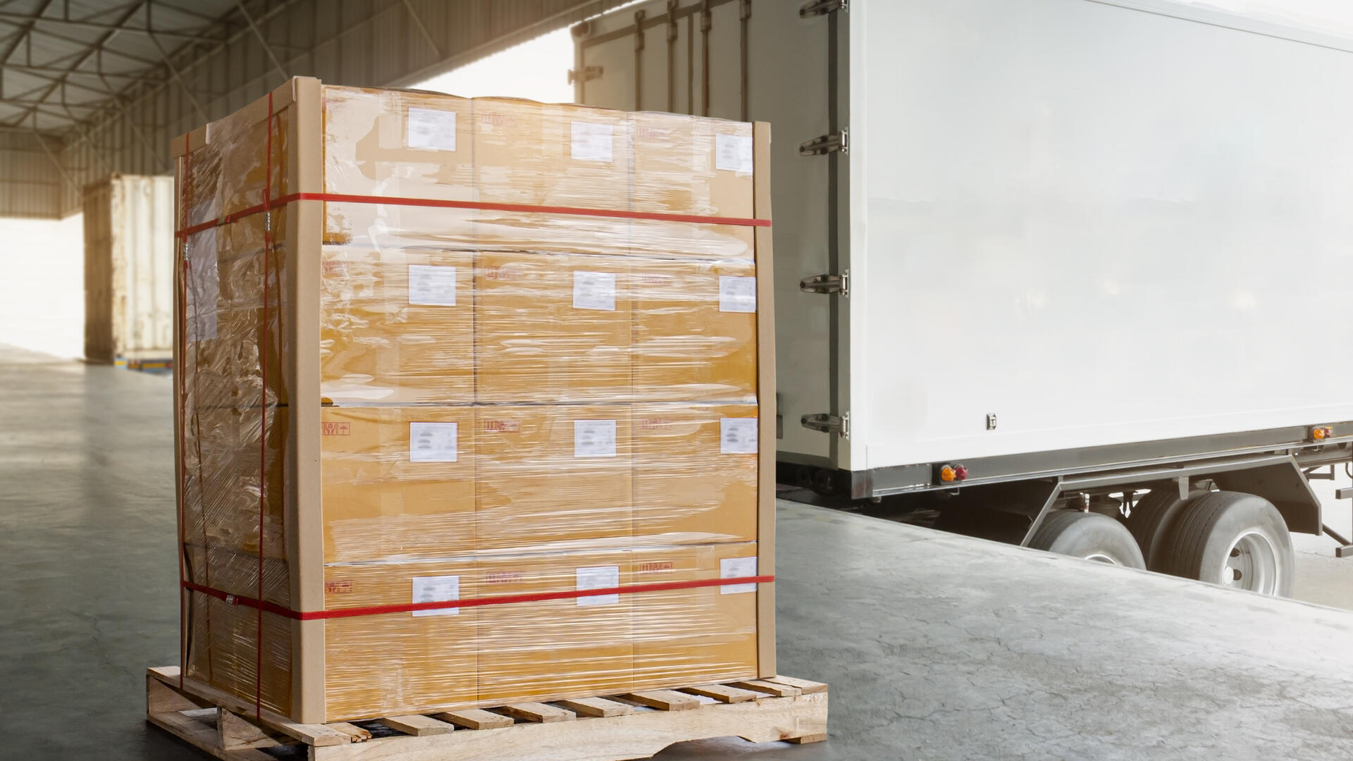 Palletized goods wrapped in plastic at a warehouse loading dock next to a delivery truck.