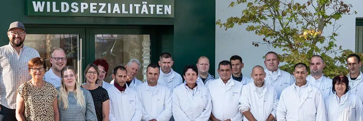 Employees of Huber in white workwear standing together outside a company building.