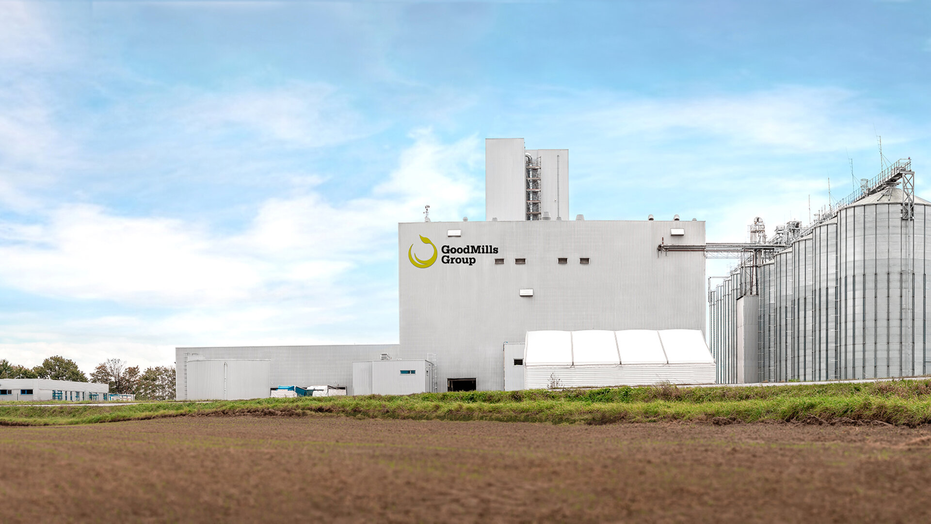 Industrial facility with silos and production buildings under a clear sky.