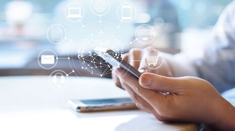 A person using a smartphone with digital icons for email, shopping, documents, and connectivity floating above, symbolizing mobile access to various online services and the digital world