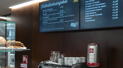 Mensa counter with bread display, coffee machine, and menu board on the wall.